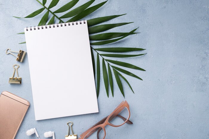 Top view of notebook with smartphone and leaves on desk