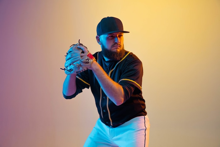 Baseball player, pitcher in a black uniform practicing and training on gradient wall in neon light. young professional sportsman in action and motion. healthy lifestyle, sport, movement concept.